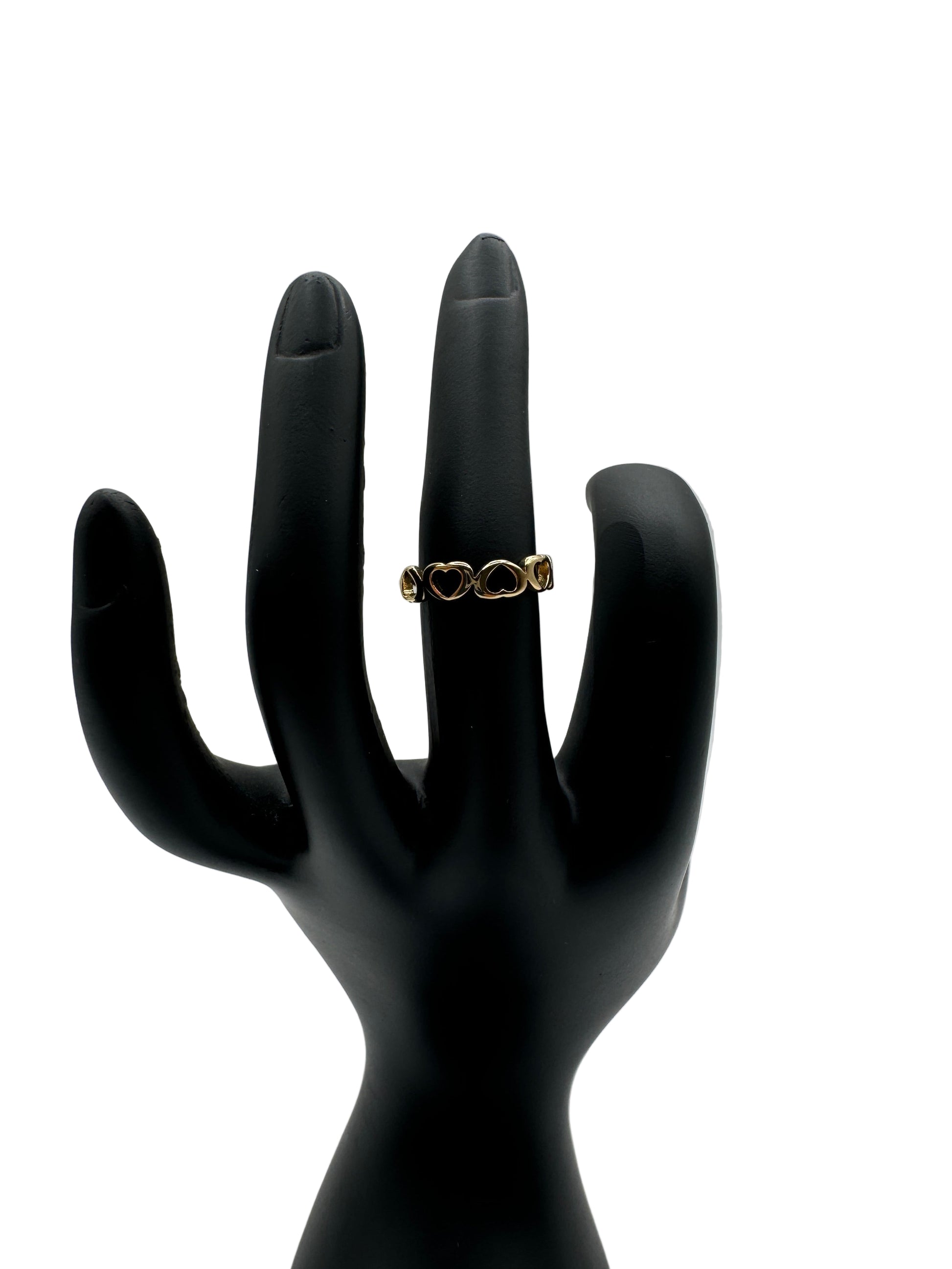 Gold ring on a black mannequin hand against a light gray background